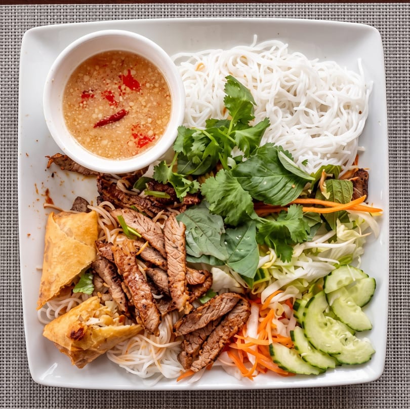 Vietnamese vermicelli bowl with grilled beef, egg rolls, fresh herbs, vegetables, and dipping sauce.