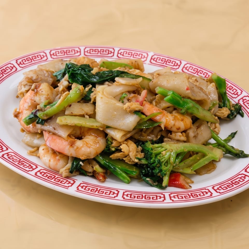 A plate of stir-fried flat noodles with shrimp, broccoli, and leafy greens.