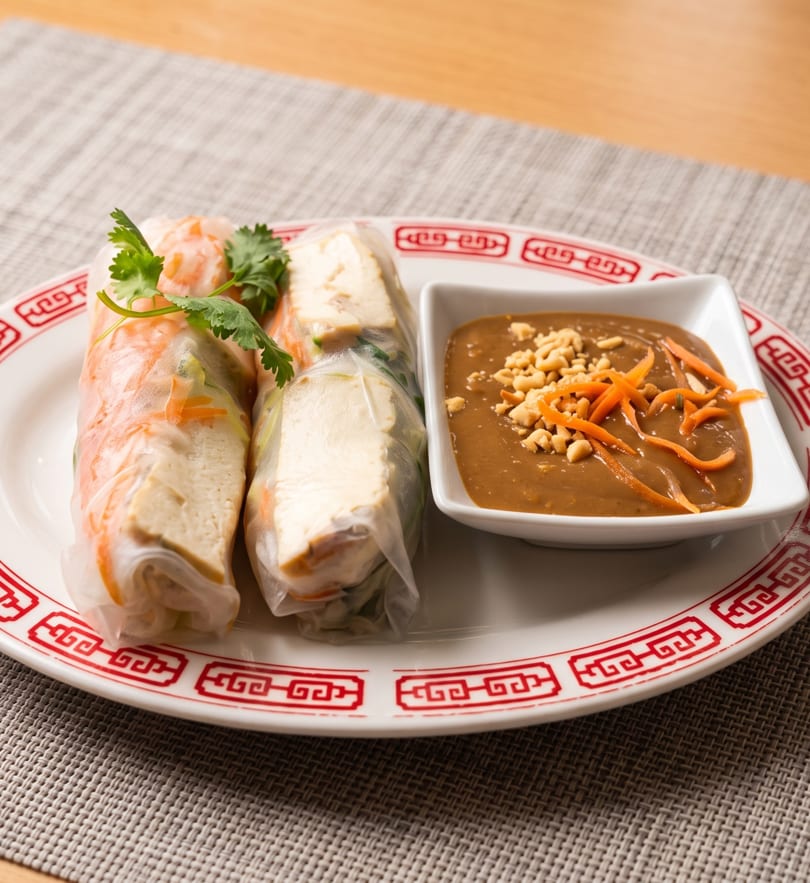 Two fresh spring rolls with shrimp and tofu, garnished with cilantro, served with peanut sauce.